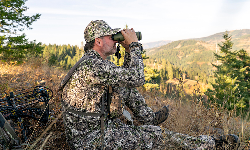 Hunter looking through binoculars over a ravine